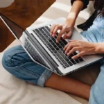 Woman browsing the web for cheap flights using the best travel websites, with a laptop on her lap.