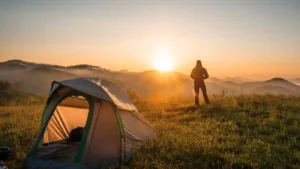 Silhouette of a man admiring the sunrise views over the mountains from a wild camping spot next to his tent.