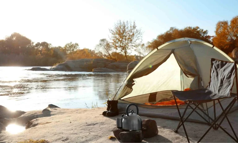 Wild camping setup by a lake, with a tent already prepared with sleeping bags, a camping chair and cooking equipment and utensils.
