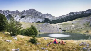 Wild camping with a view of the mountains with two tents set up by a lake.