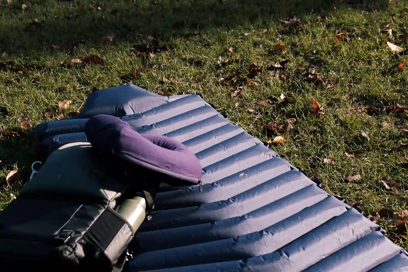 The rolled out LayOn Air Sleeping Pad next to a medium sized backpack for size comparison.
