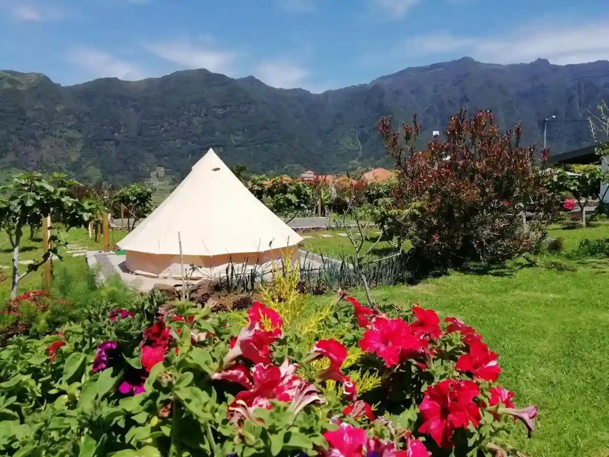 A glamping tent in green field with red flowers in the foreground and mountains in the background. 