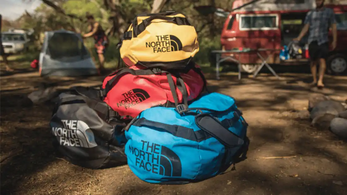 A pile of The North Face Duffels in blue, red, yellow and black.