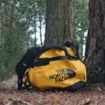 The North Face Duffel in yellow and black on the forest floor.