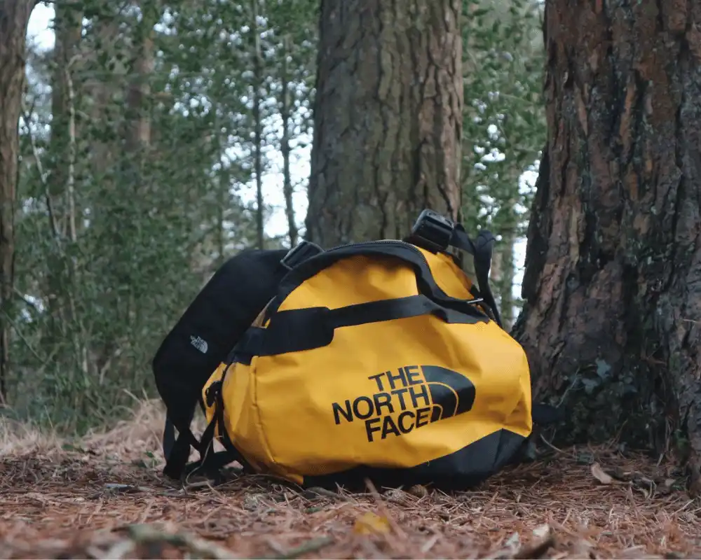 The North Face Duffel in yellow and black on the forest floor.