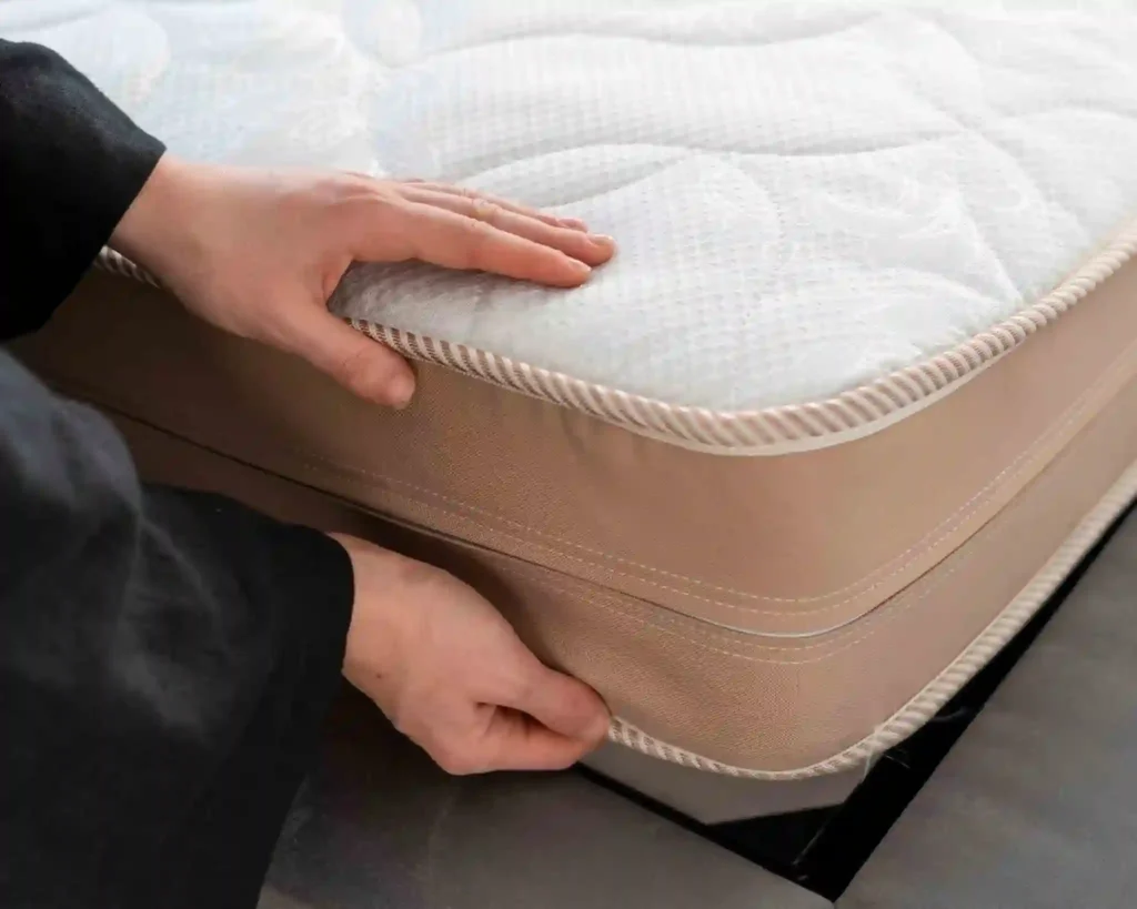 A person lifts a mattress from the bed frame.