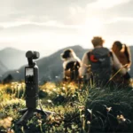 A A DJI Osmo Pocket 3 set in the grass, while two people and a dog can be seen in the foreground.